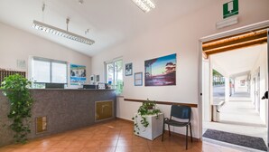 A reception area with a counter, a chair, a potted plant, and a painting on the wall. - Autohotel (Formello)