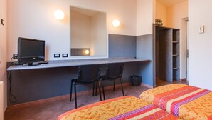 A hotel room with a desk, two chairs, a bed with patterned bedding, a large mirror, and a wardrobe. - Autohotel (Formello)