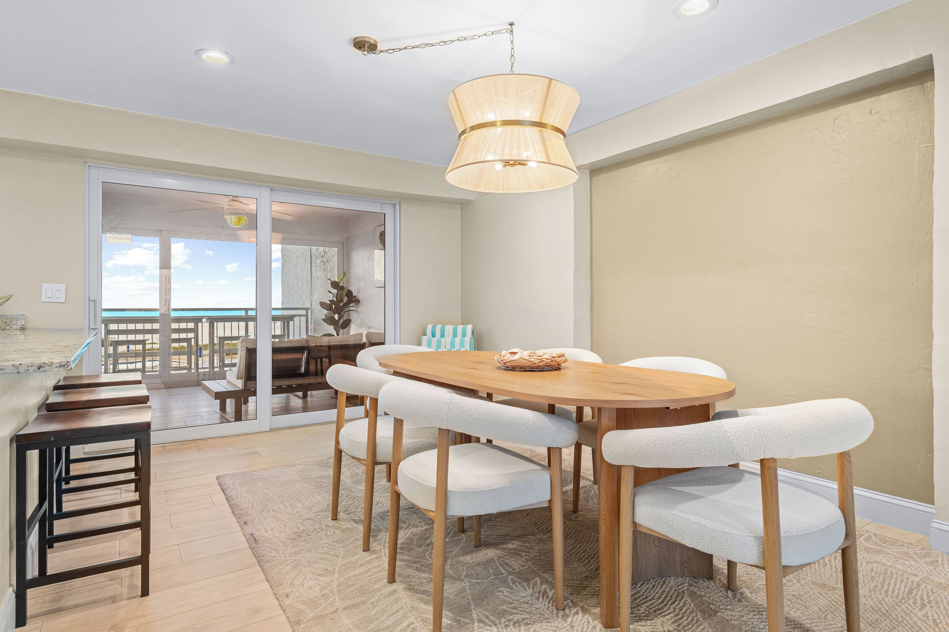 Un coin repas avec une table et des chaises en bois, un luminaire suspendu et une vue sur un balcon extérieur, accessible par une porte vitrée.
