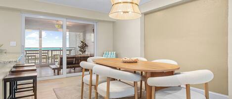 Un coin repas avec une table et des chaises en bois, un luminaire suspendu et une vue sur un balcon extérieur, accessible par une porte vitrée.