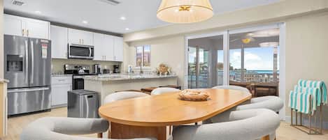 A modern kitchen with stainless steel appliances, a dining area with a wooden table and chairs, and a view through glass doors.