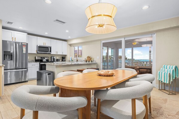 A modern kitchen with stainless steel appliances, a dining area with a wooden table and chairs, and a view through glass doors.