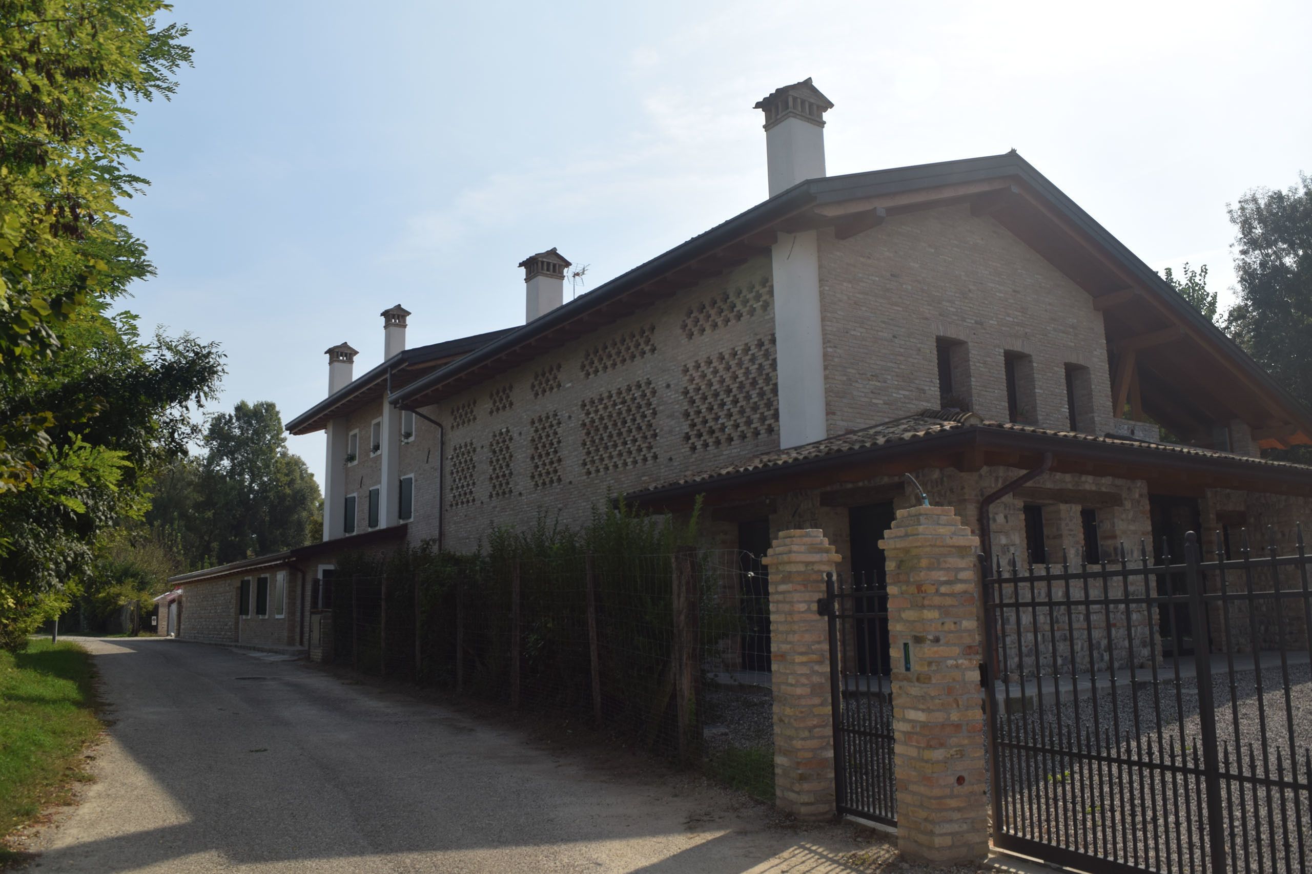 Un bâtiment à deux étages avec une façade en briques, un porche couvert et une allée d’accès fermée par un portail.
