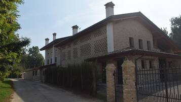 Un bâtiment à deux étages avec une façade en briques, un porche couvert et une allée d’accès fermée par un portail.