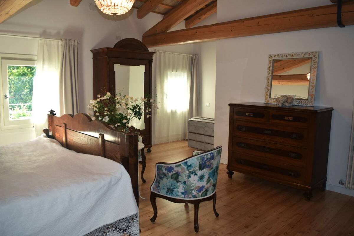 A bedroom with a wooden bed, a dresser, a chair, and a large mirror.