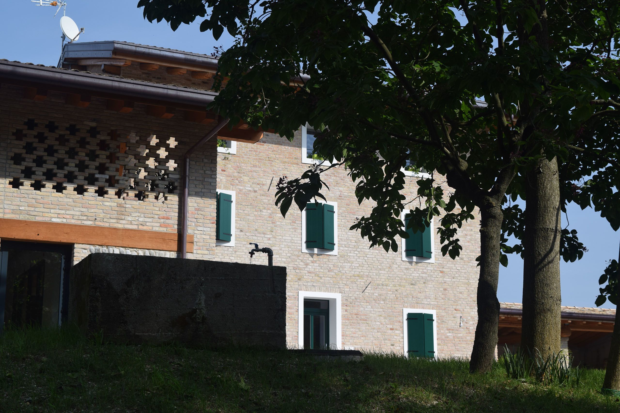 A brick building with green shutters, a satellite dish, and a tree in the foreground.
