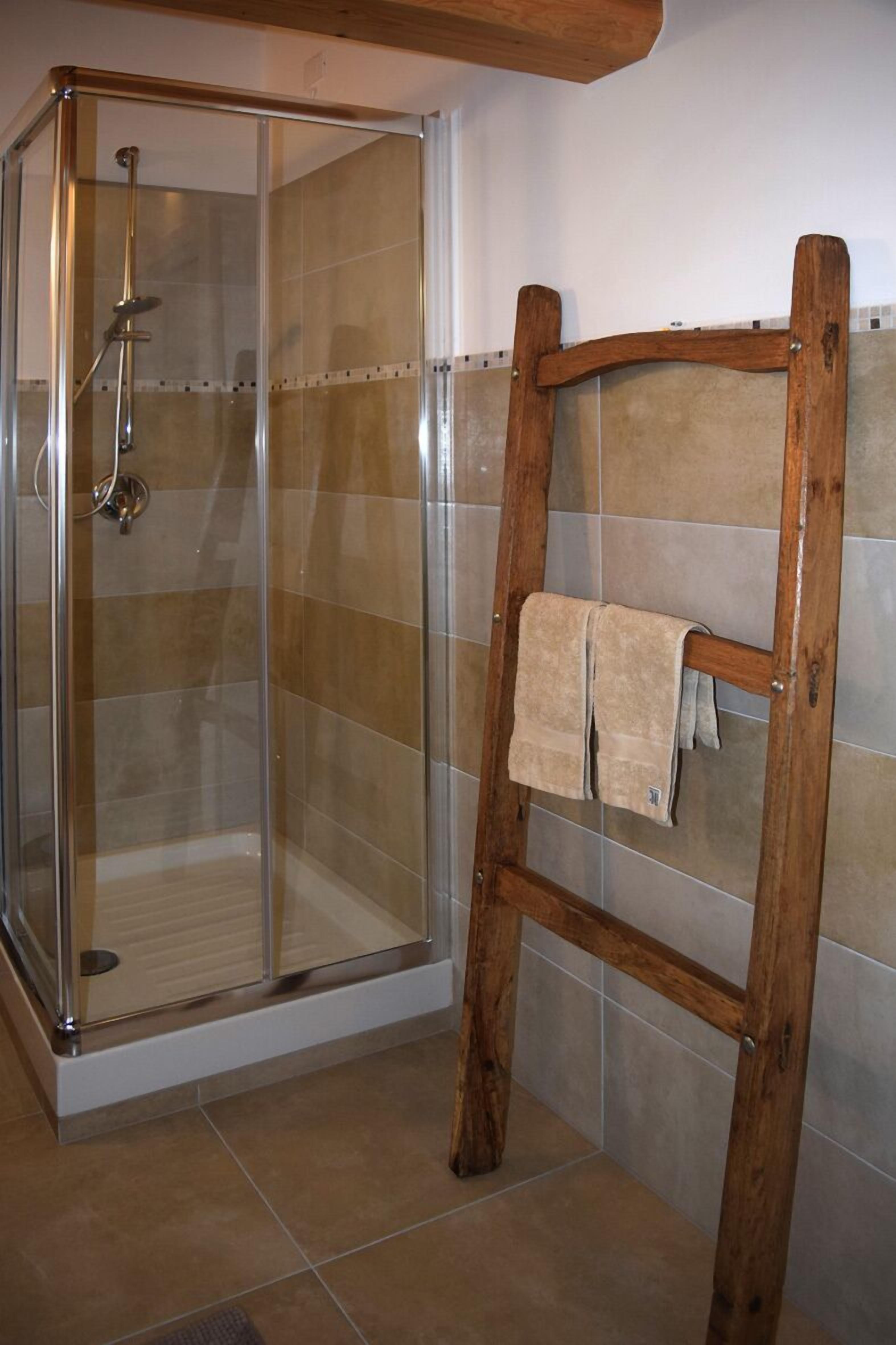 Een douche met een glazen deur en een houten handdoekrek met handdoeken.
