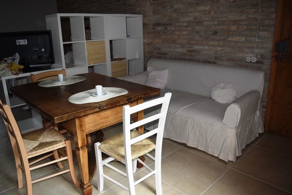 A cozy living room with a wooden dining table, white chairs, a white sofa, and a brick wall.