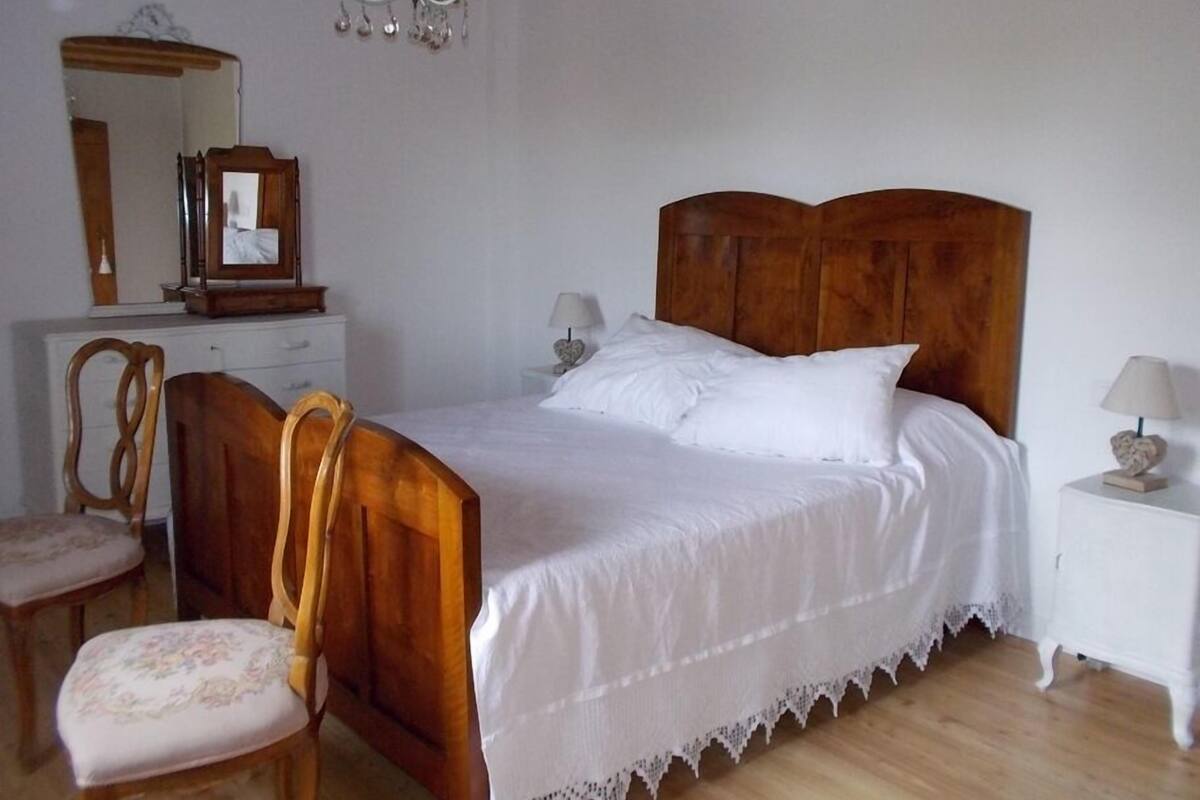 A bedroom with a wooden bed, a wooden chair, a dresser, a mirror, and a chandelier.