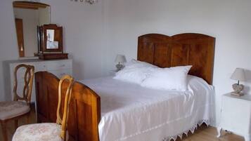 Un dormitorio con cama y silla de madera, cómoda, espejo y candelabro.