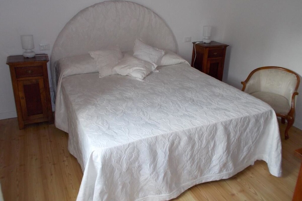 A bedroom with a large bed, two bedside tables, a chair, and a wooden floor.