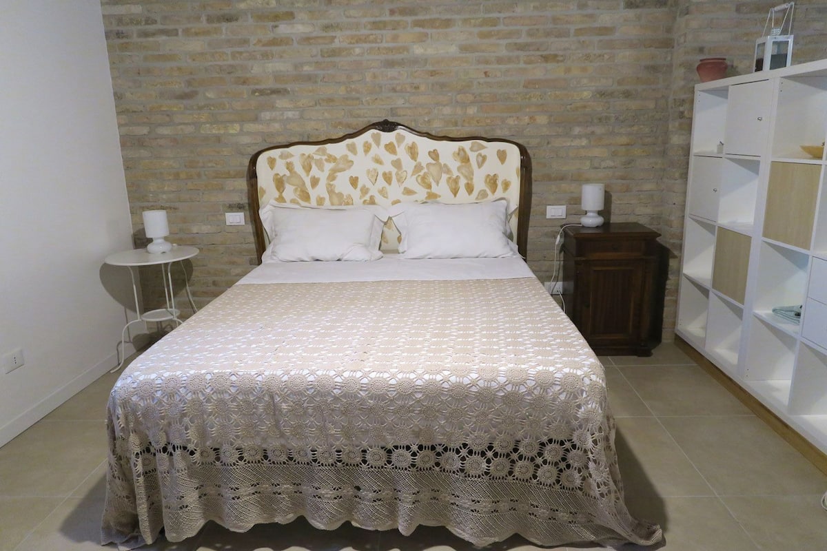 A bed with a patterned bedspread, a bedside table with a lamp, and a wardrobe with shelves.