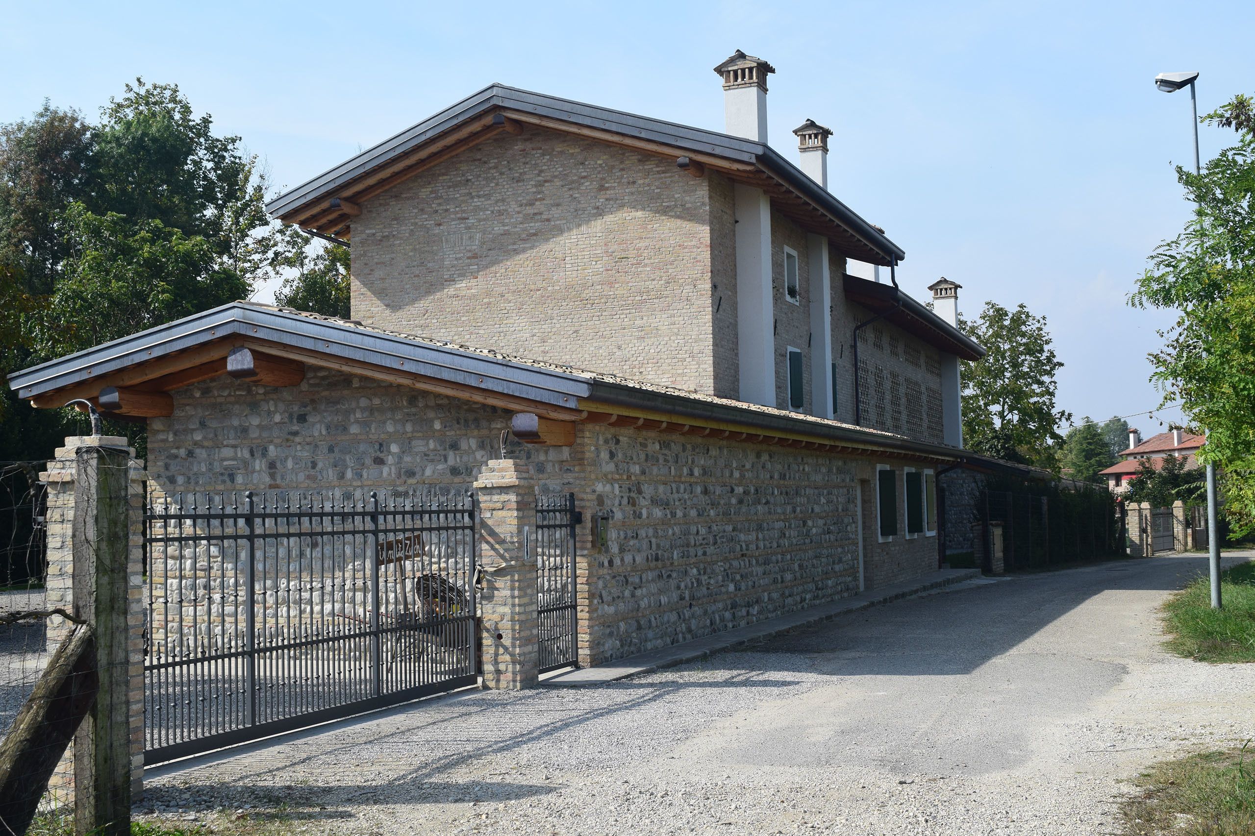 Un edificio in pietra su due piani con un cancello in metallo e un vialetto sterrato.