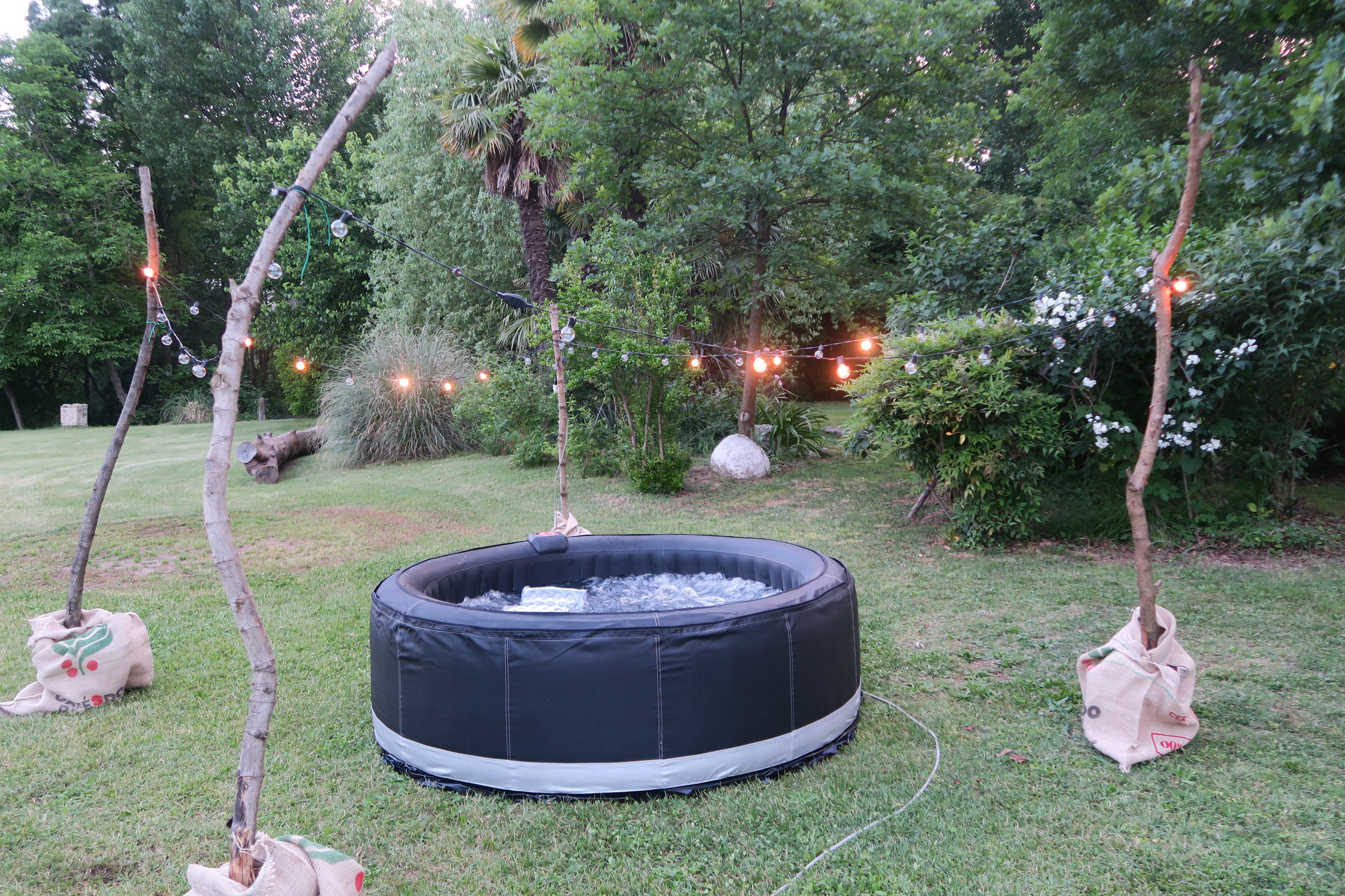 An inflatable pool surrounded by trees and grass, with string lights in the background.