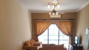 A spacious living room with a large glass table surrounded by green chairs, a sofa, and a ceiling fan. - Ideal Holiday Apartment Marina Court (Kota Kinabalu)