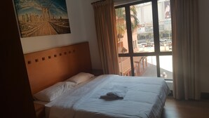 A hotel room with a bed, a painting of a cityscape, and a view of the street outside. - Ideal Holiday Apartment Marina Court (Kota Kinabalu)