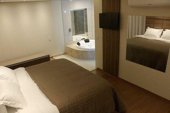 Ein Hotelzimmer mit einem großen Bett, einem separaten Badezimmer mit Badewanne und einem an der Wand montierten Flachbildfernseher.