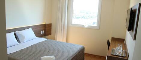 A hotel room with a bed, a bedside table with a glass, and a window with curtains.
