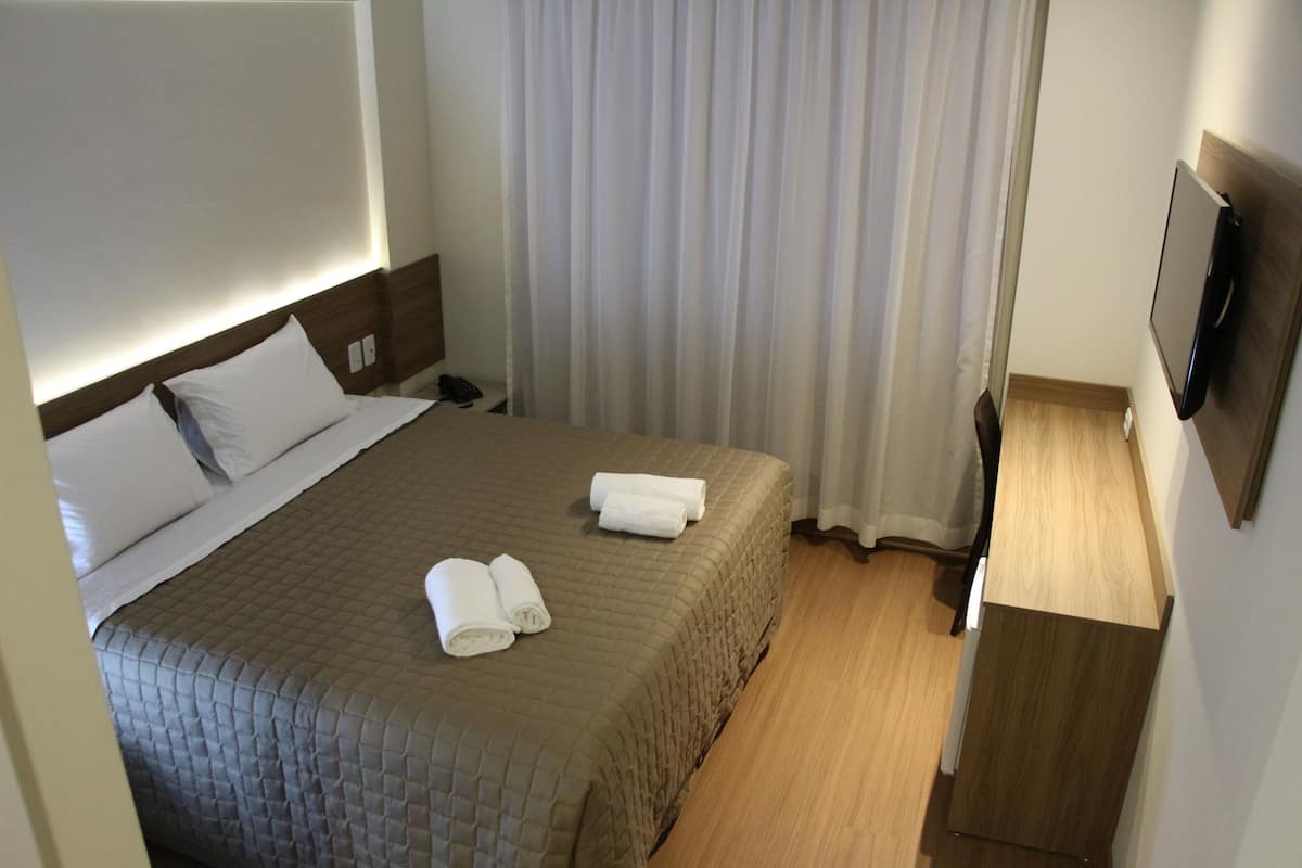 Une chambre d’hôtel avec un lit, une table de chevet, une télévision et un rideau.