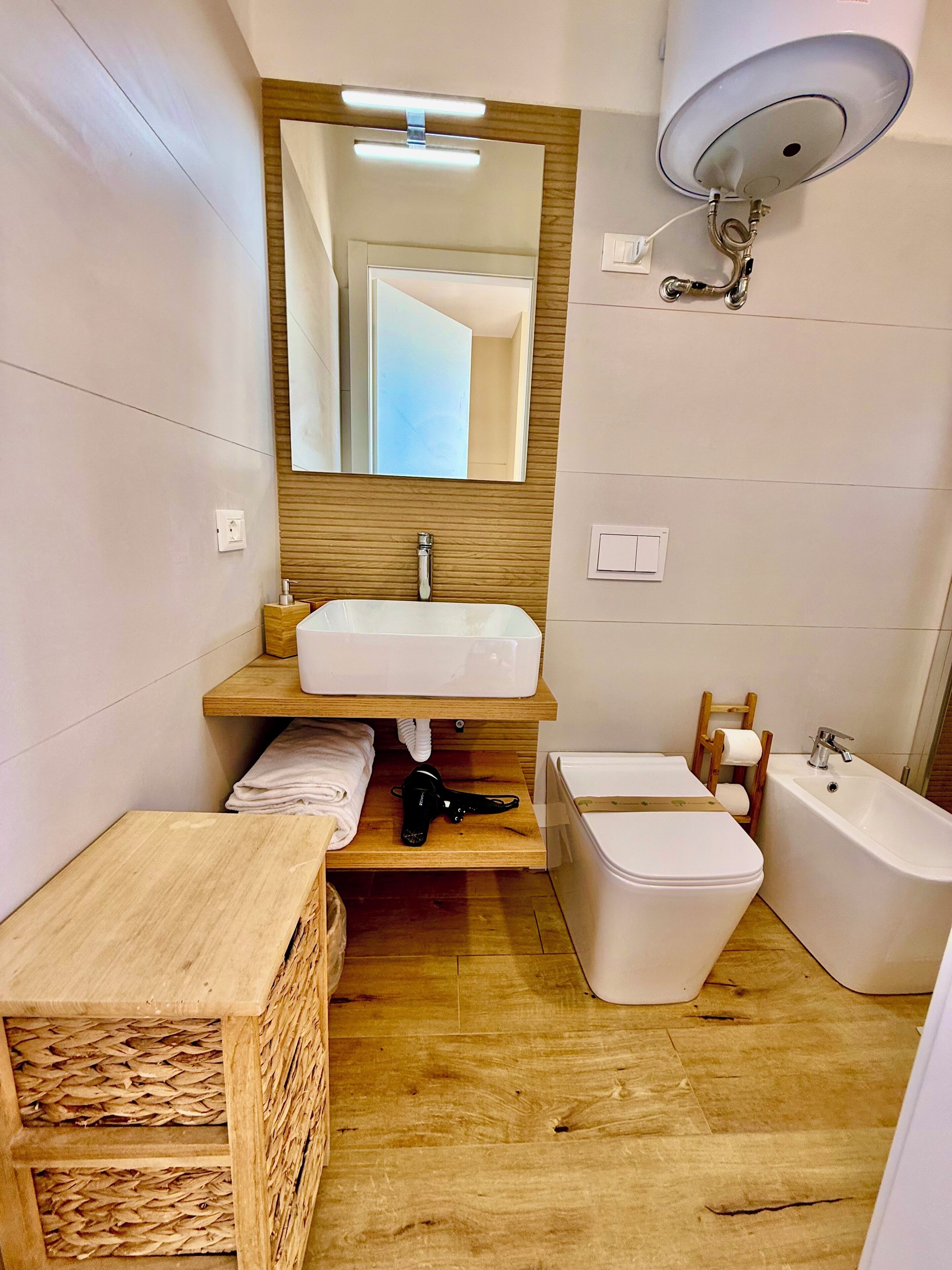 Un baño moderno con tocador de madera, un espejo grande, inodoro, bañera y perchero para toallas.