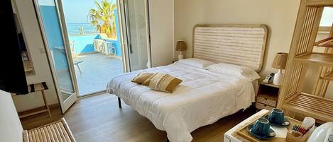 A bedroom with a bed, bedside table, lamp, and a view of the ocean.