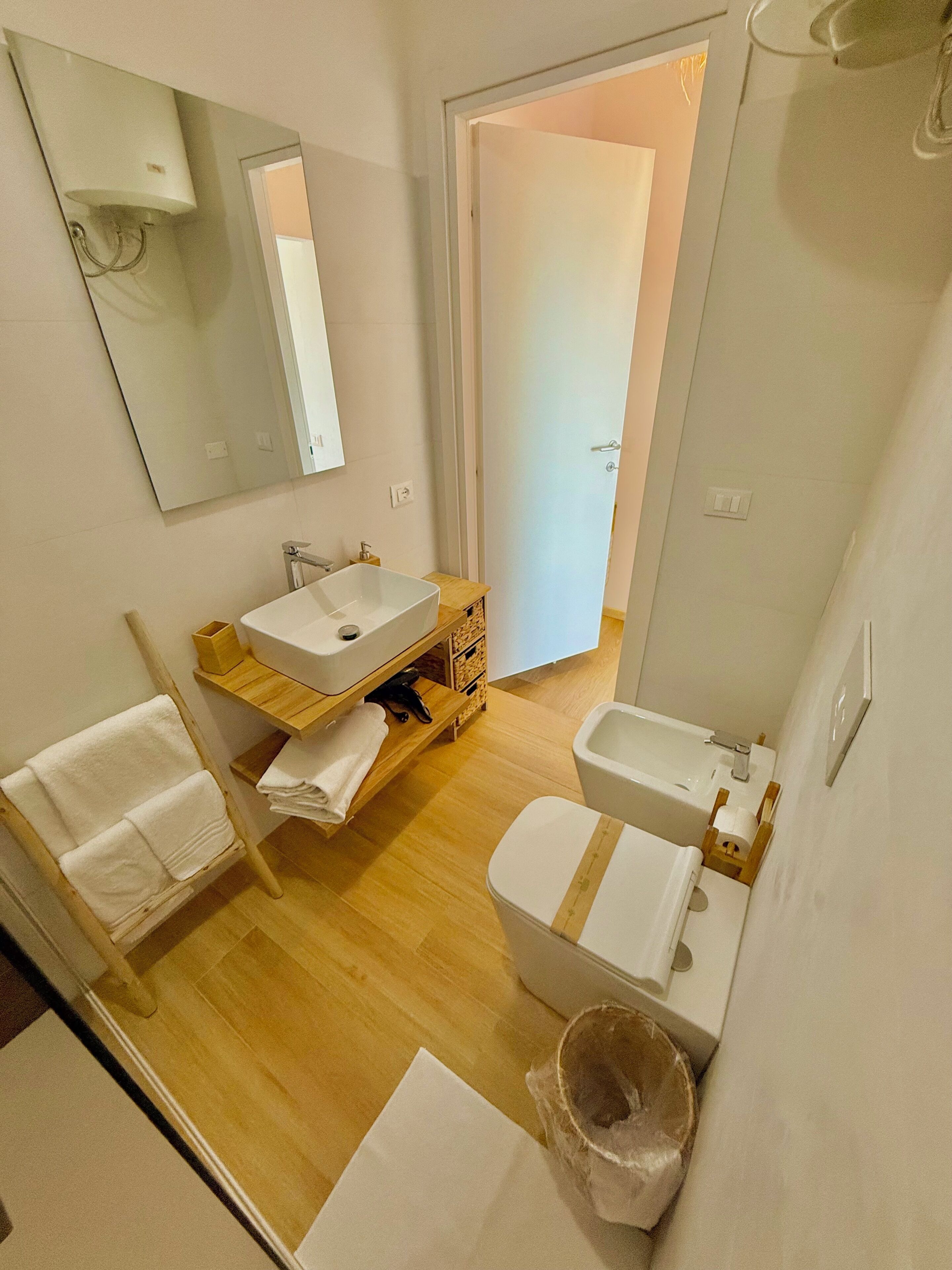 Un baño pequeño con tocador de madera, un espejo grande, un lavabo blanco y un inodoro.