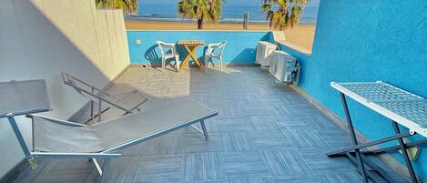Terraza en la azotea con vista a la playa, que incluye una mesa y sillas, una hamaca y un área junto a la piscina.