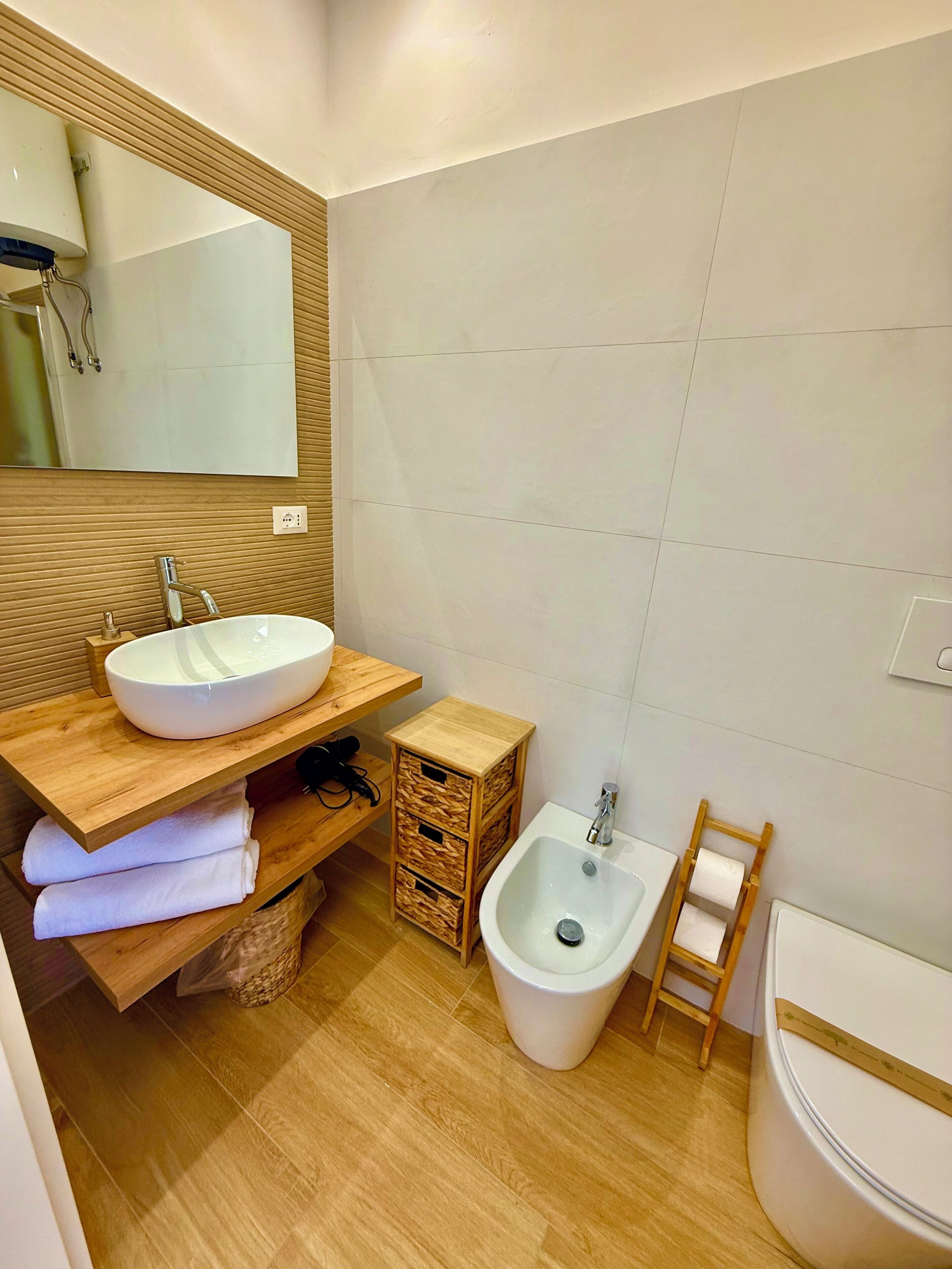 Un baño moderno con tocador de madera, un espejo grande, un lavamanos blanco, un bidé y un inodoro.