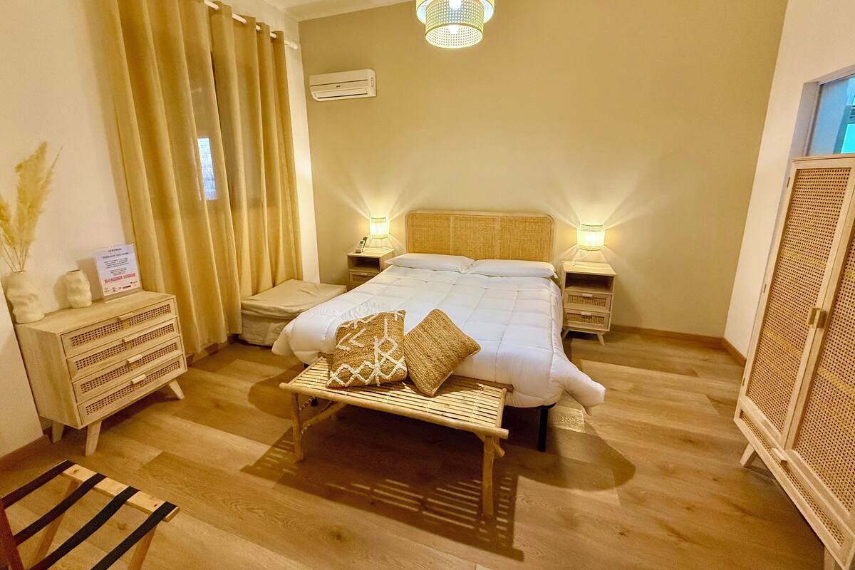 Une chambre à coucher comprenant un lit, des lampes de chevet, un banc, une armoire et un luminaire au plafond.