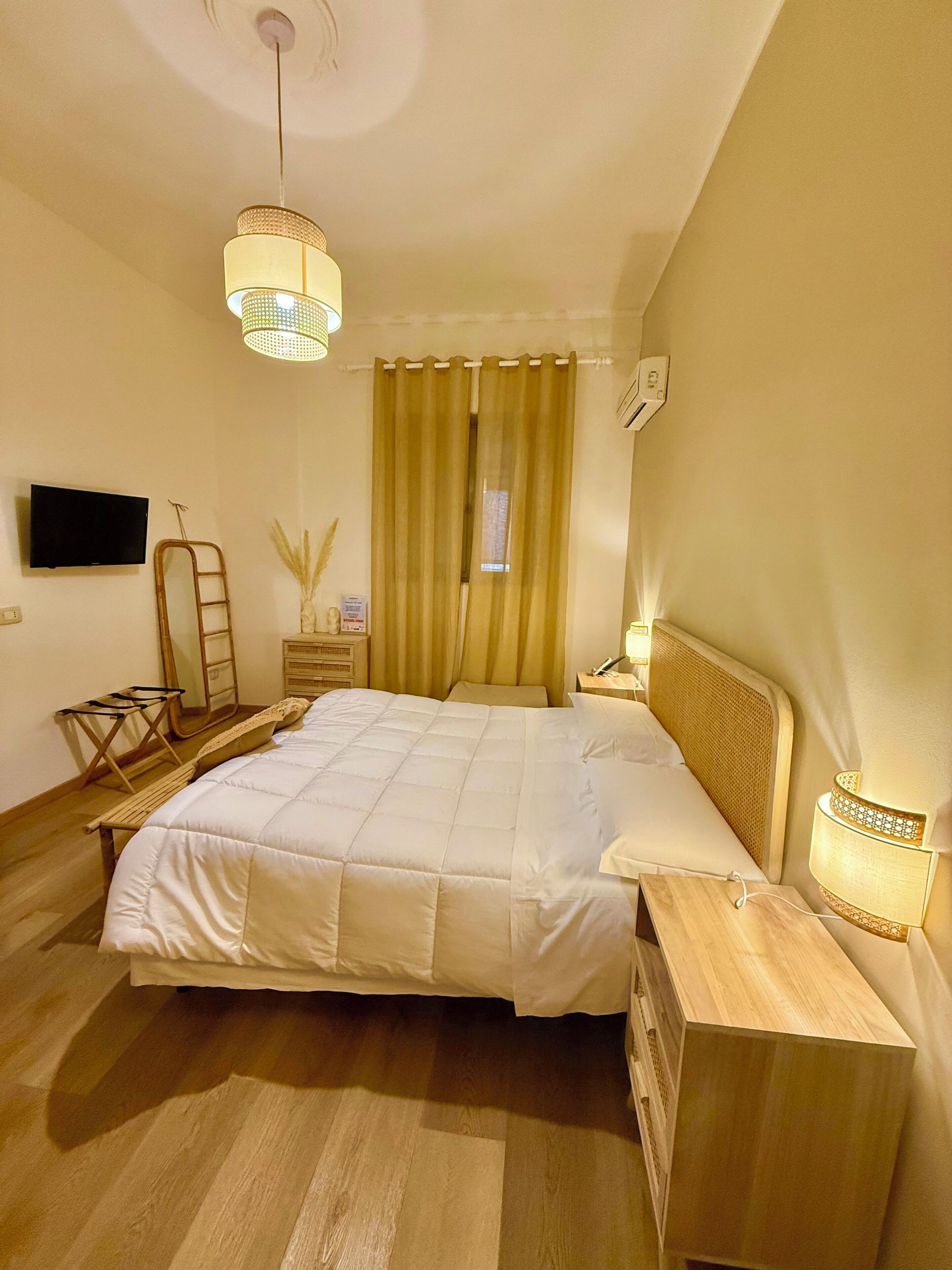 A bedroom with a bed, bedside tables, a TV, and a window with curtains.