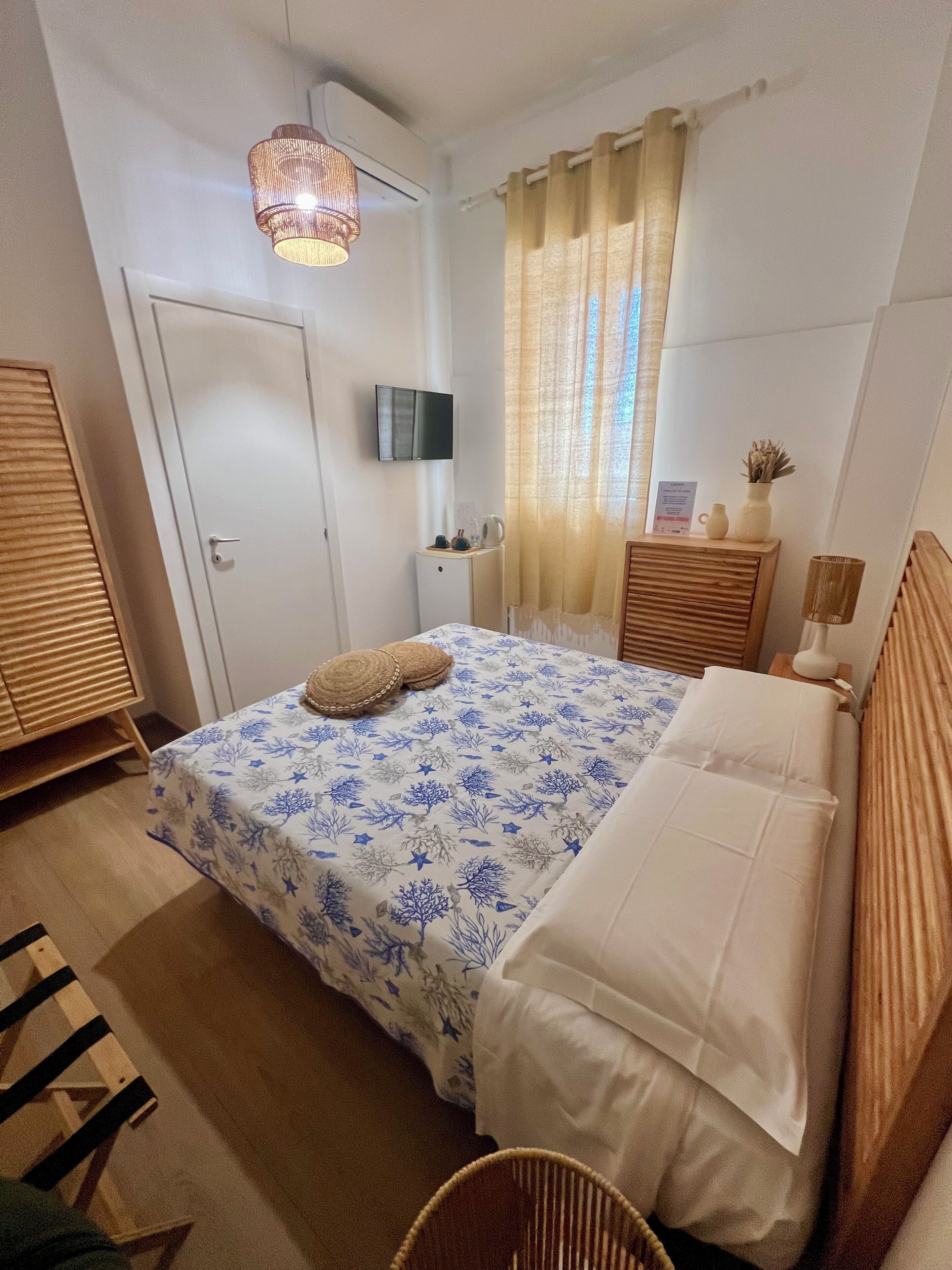 A bedroom with a bed, a television, a small table, a chair, and a window with curtains.