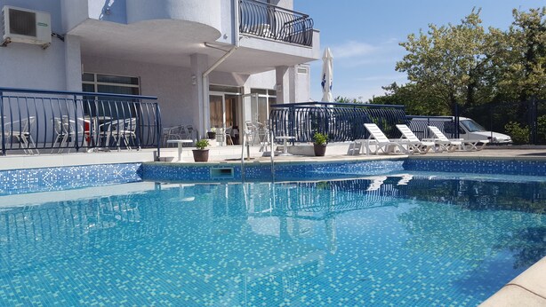 Una piscina con bordi piastrellati, sedie a sdraio e un edificio con un balcone sullo sfondo.