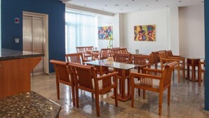 Un'area pranzo moderna con sedie in legno e un tavolo in vetro, pareti blu e due quadri colorati.