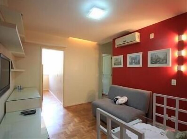 Ein Zimmer mit roter Akzentwand, einem grauen Sofa, einer weißen TV-Konsole und einem Flur, der in ein weiteres Zimmer führt.