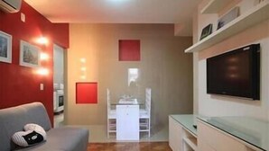 A compact living space with a grey sofa, a flat-screen TV mounted on the wall, and a small kitchenette area. - GoHouse Djalma 401 A (Rio de Janeiro)