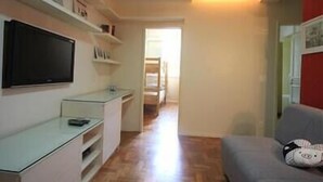 A compact living space with a flat-screen TV mounted on the wall, a small glass table, and a grey sofa with a cushion. - GoHouse Djalma 401 A (Rio de Janeiro)