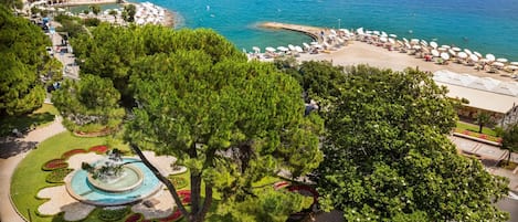 Une zone côtière comprenant une plage, une fontaine et un parc avec des arbres et des parterres de fleurs.