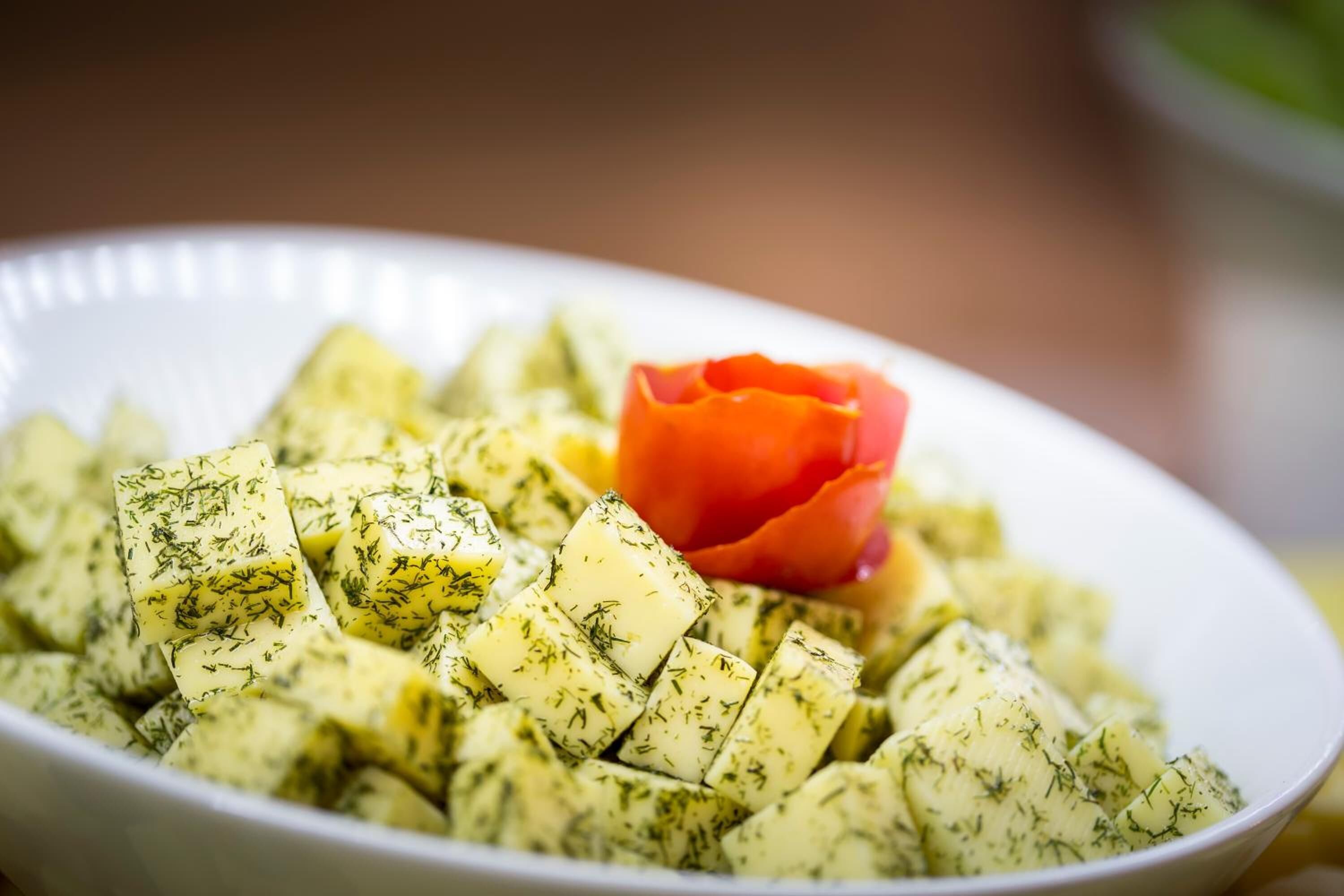 A bowl of potato salad with dill and a tomato garnish.