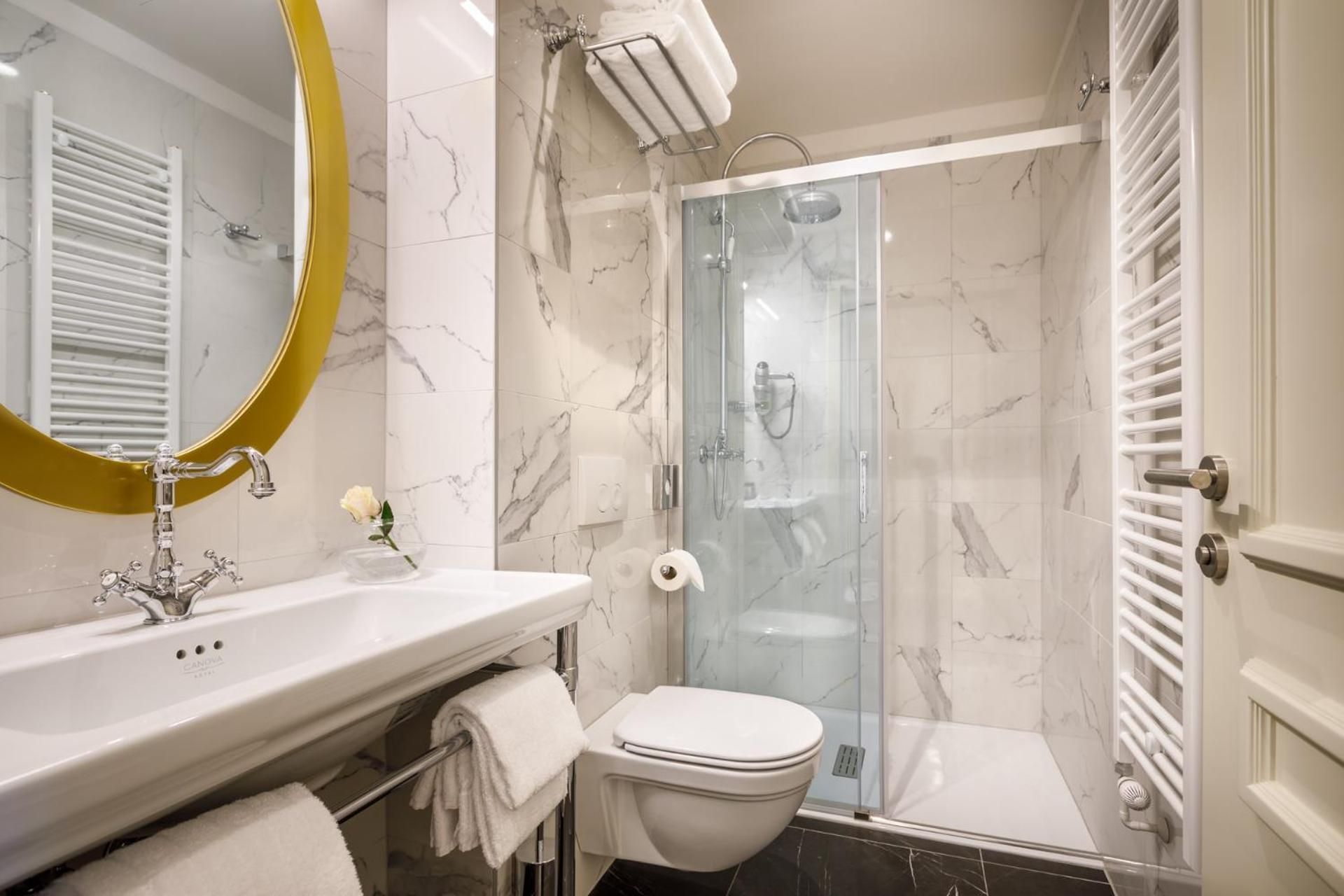 Une salle de bain avec une douche à parois de verre, des toilettes blanches, un lavabo avec un miroir et un porte-serviettes.