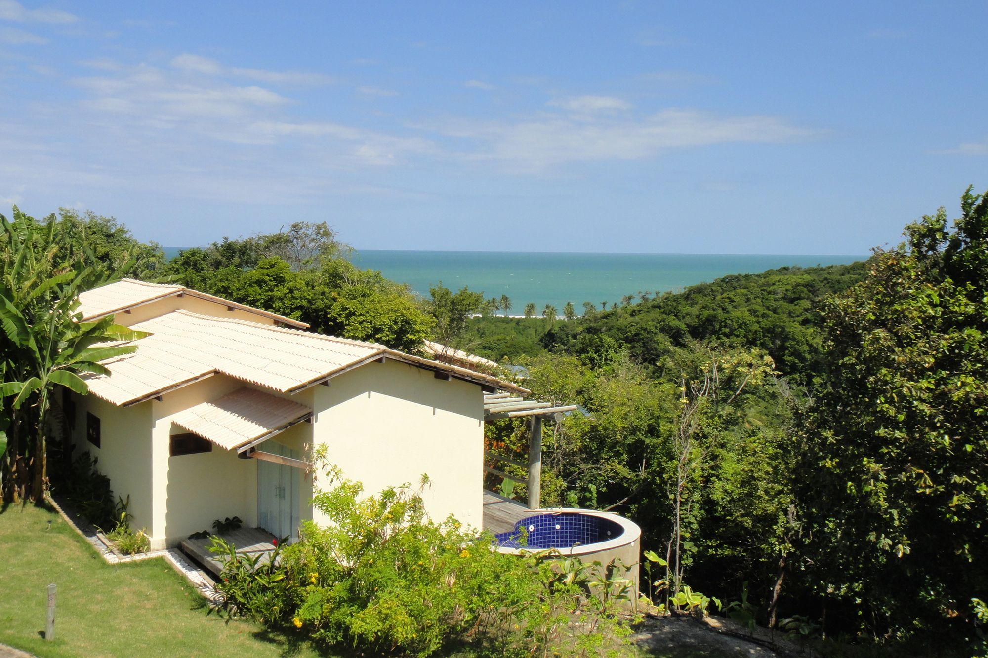 A house with a swimming pool, surrounded by lush greenery and overlooking a beach.