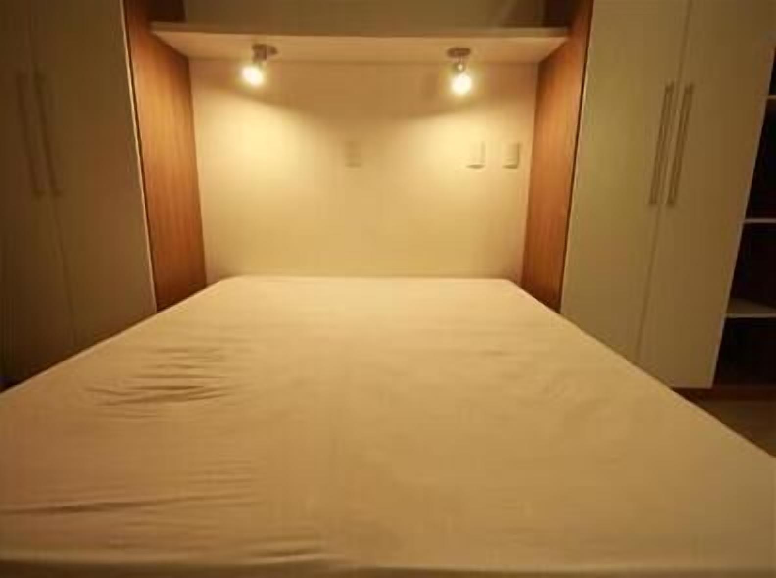 Una stanza piccola e stretta con un letto, due luci a parete e mobili in legno.