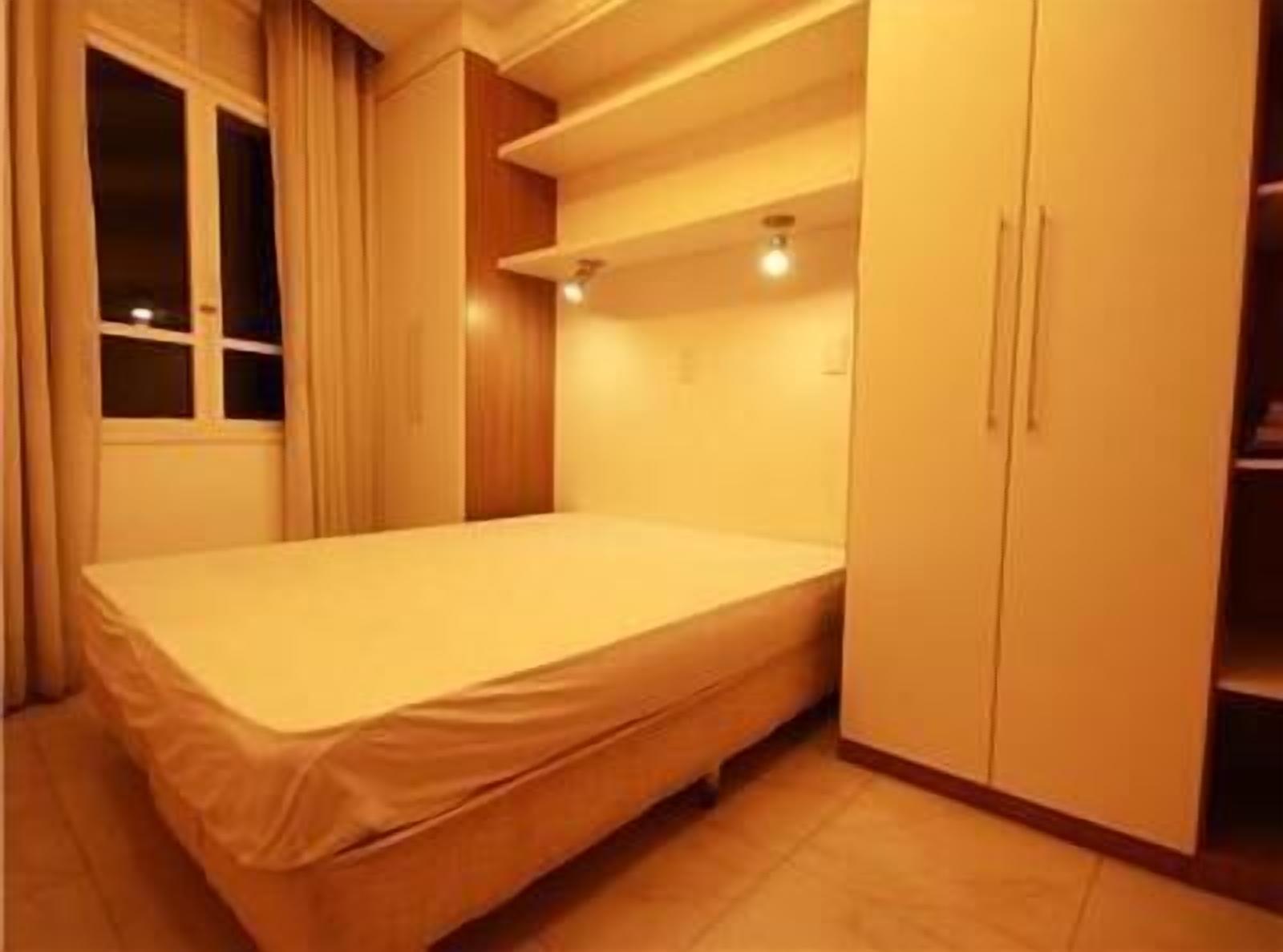 A small, neatly arranged bedroom with a single bed, a window, and built-in storage cabinets.