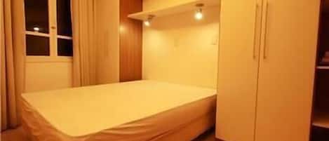 A small, neatly arranged bedroom with a single bed, a window, and built-in storage cabinets.