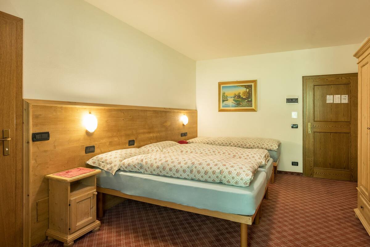 A bedroom with two beds, wooden headboard, bedside tables, a nightstand, a painting, and a door with a lock.