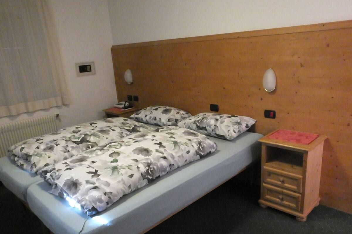 A single bed with floral bedding, a wooden headboard, bedside tables with lamps, and a small wooden cabinet.