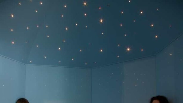 Une pièce dont le sol et les murs sont recouverts de carreaux bleus, avec un espace détente comprenant des bancs, et un plafond orné de petites lumières.