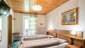 Une chambre avec deux lits, une tête de lit en bois, une table de chevet avec une lampe, un tableau au mur et une vue sur l’extérieur par une fenêtre.