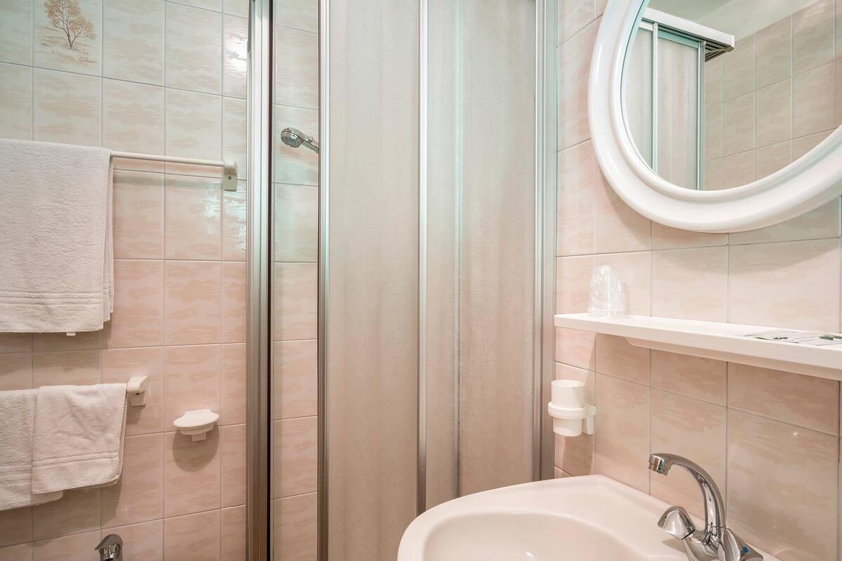 A bathroom with a glass shower enclosure, a sink with a modern faucet, a towel rack, and a mirror with a round frame.