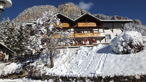 Un bâtiment doté d’un balcon en bois et de murs en pierre, entouré d’arbres et de montagnes couverts de neige.