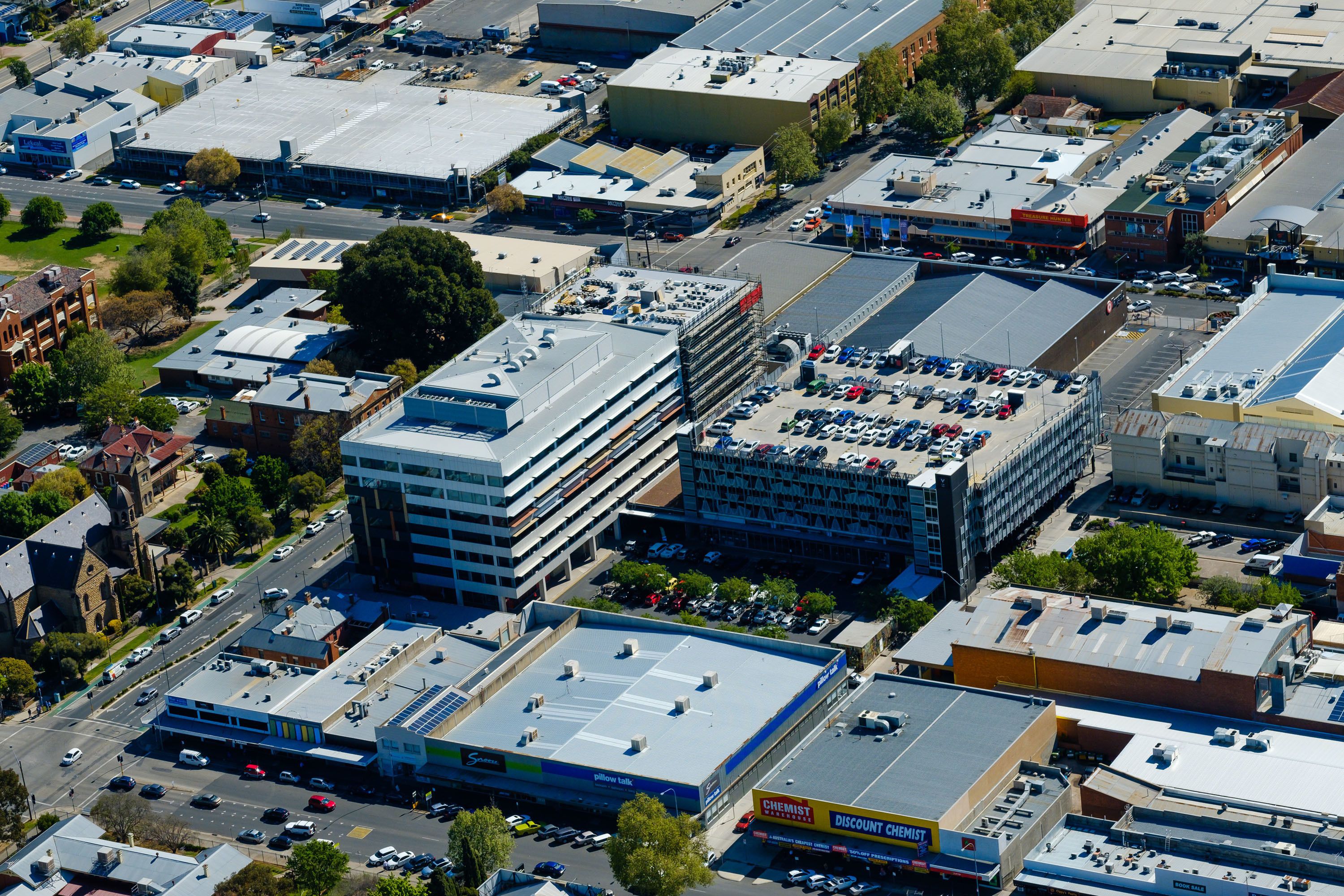 An aerial view of a commercial area with multiple buildings, including a large parking lot and a business with a sign reading "CHEMIST."